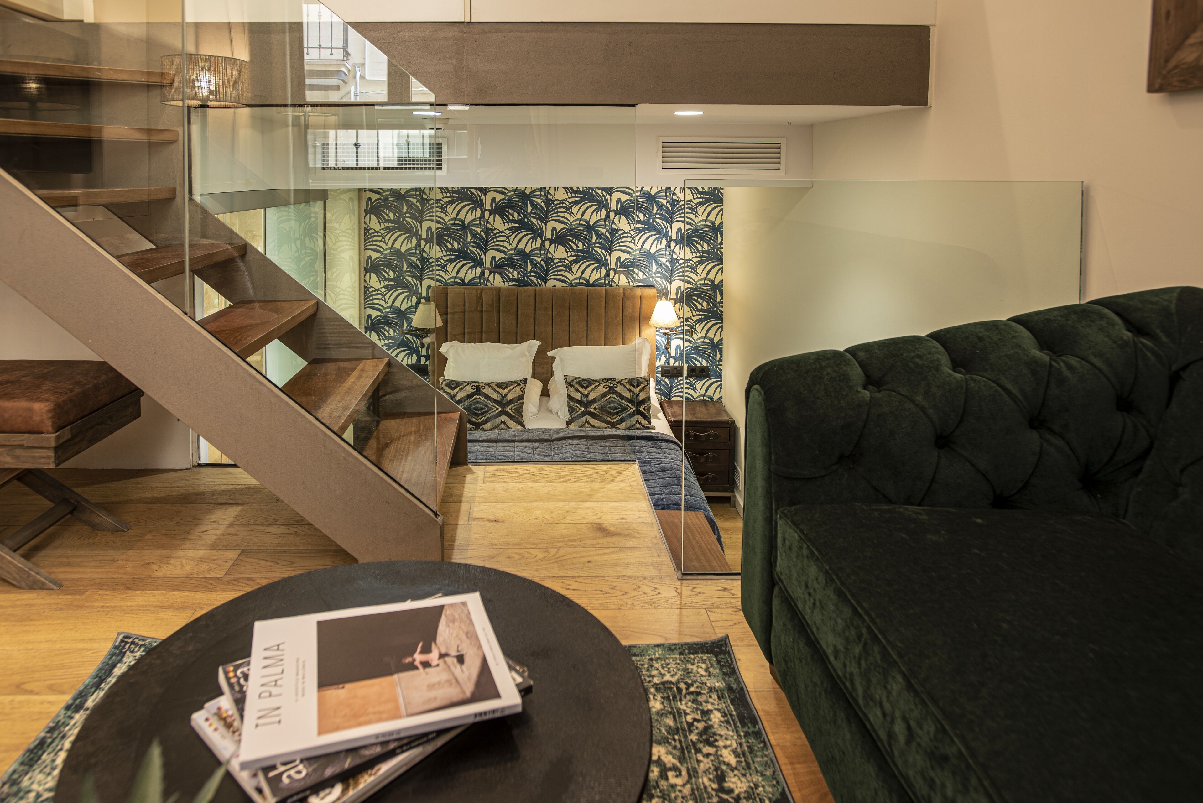 Una sala de estar moderna con una escalera, un sofá verde, piso de madera y una pared con diseño.