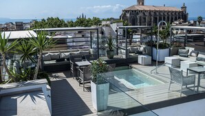 Une terrasse sur le toit avec une piscine, des espaces de détente en plein air et une vue sur un bâtiment historique.