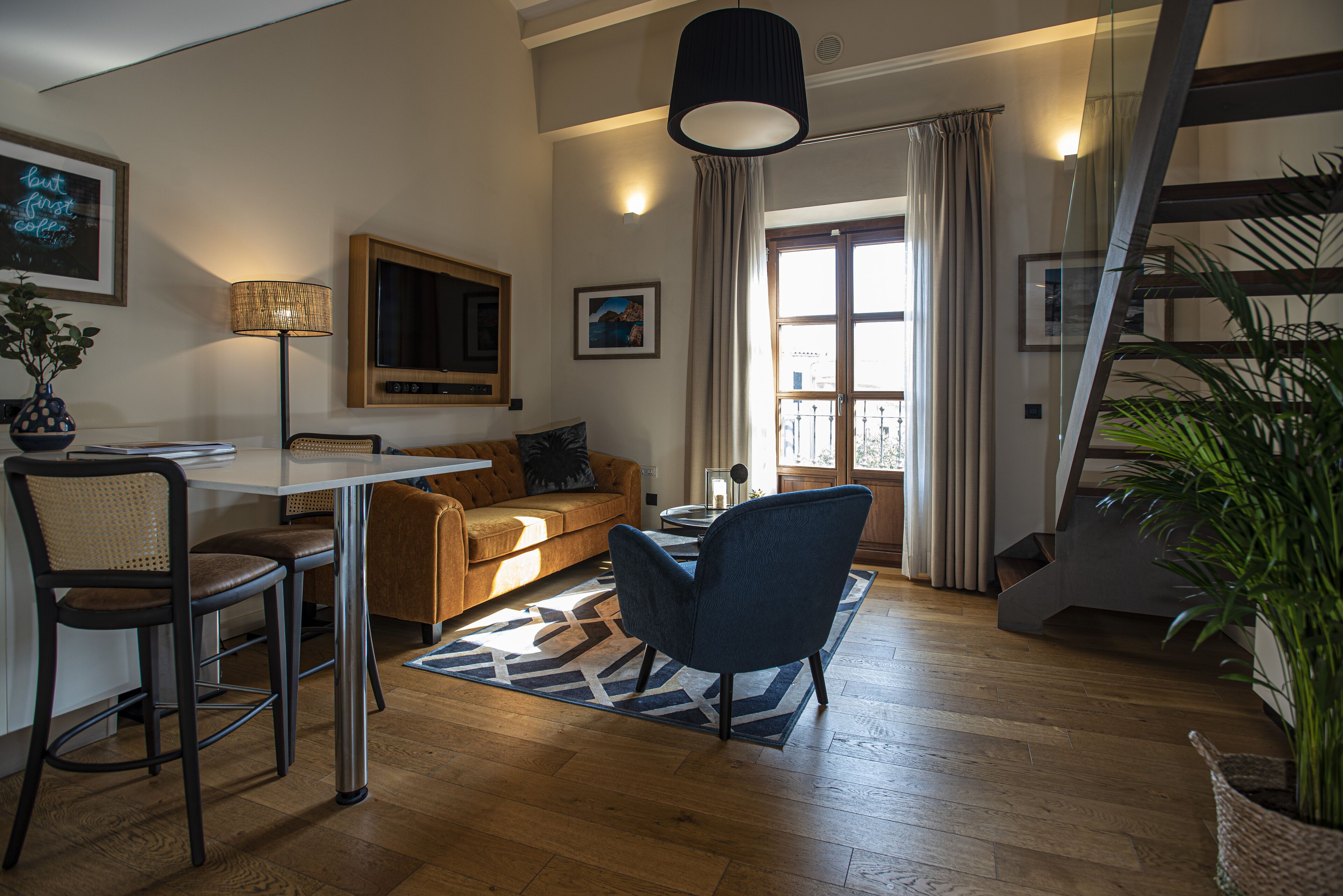 Un salon moderne avec un canapé, une table basse et des fauteuils. Un escalier mène à un niveau supérieur.