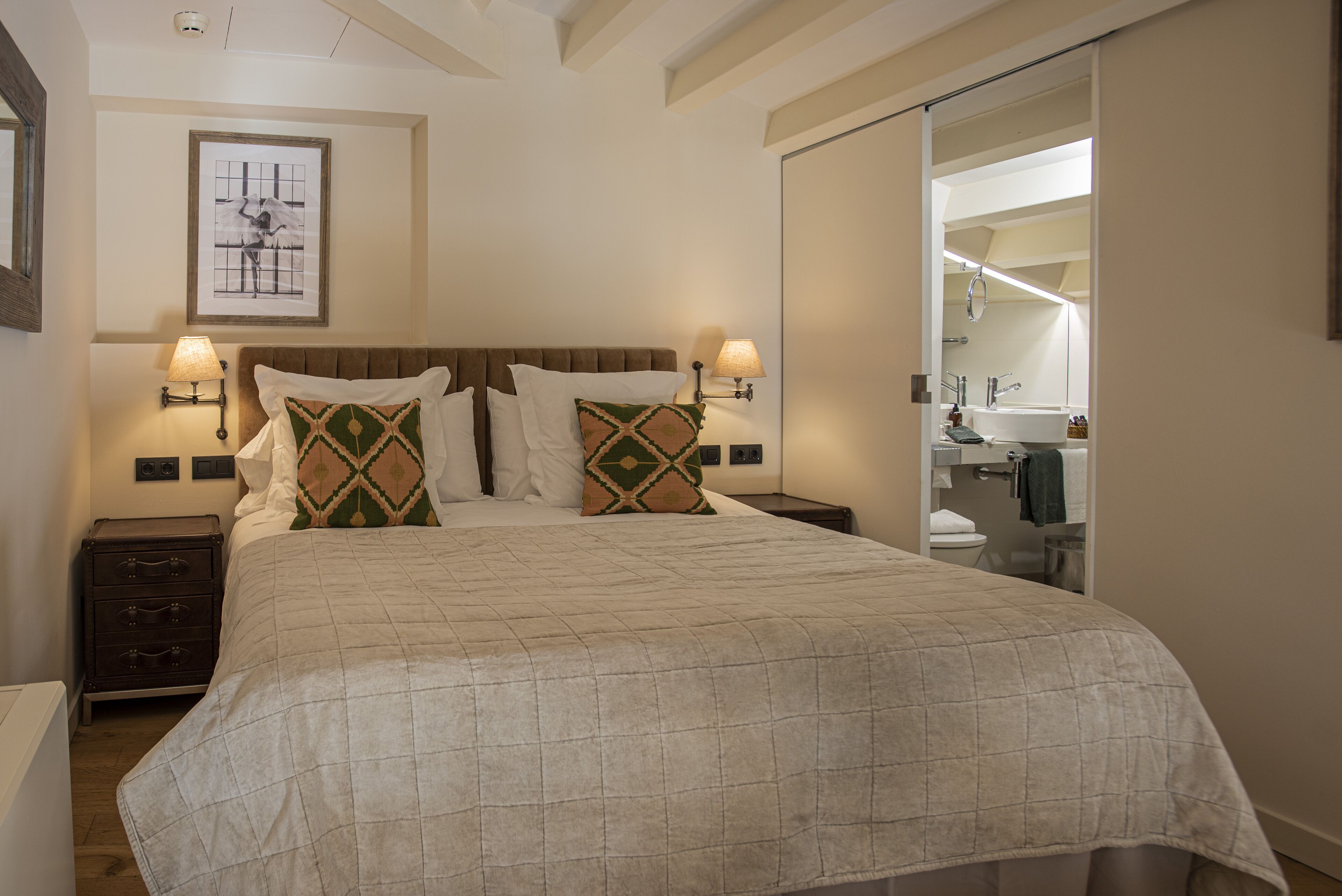 A neatly made bed with a quilted cover, two bedside lamps, and a framed artwork on the wall.
