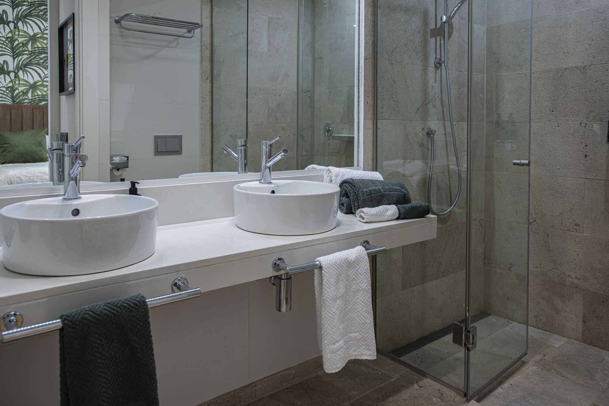 Une salle de bain moderne avec deux vasques, une douche à l’italienne en verre et un grand miroir.