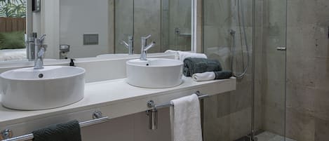 A modern bathroom with two sinks, a glass shower enclosure, and a large mirror.