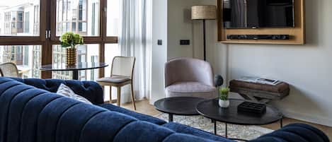 A modern living room with a blue sofa, a round coffee table, a TV mounted on the wall, and a floor lamp.