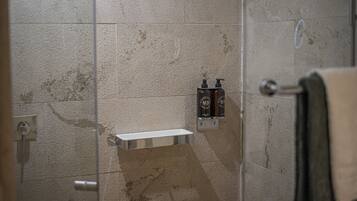 A bathroom with a glass shower enclosure, a white towel rack, and two bottles of shampoo on a wall-mounted shelf.