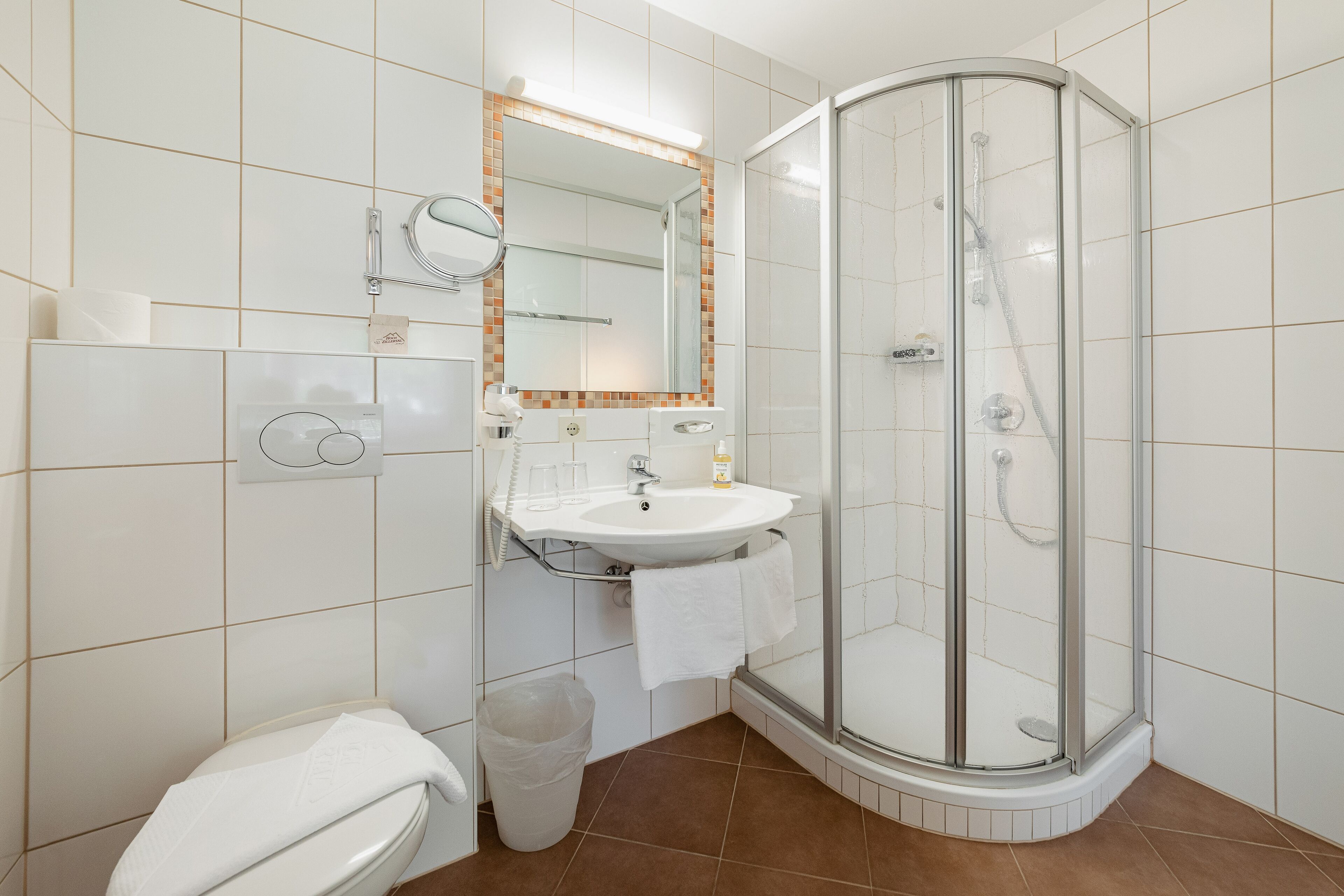 Un baño moderno con ducha envuelta en vidrio, lavamanos con espejo y retrete.