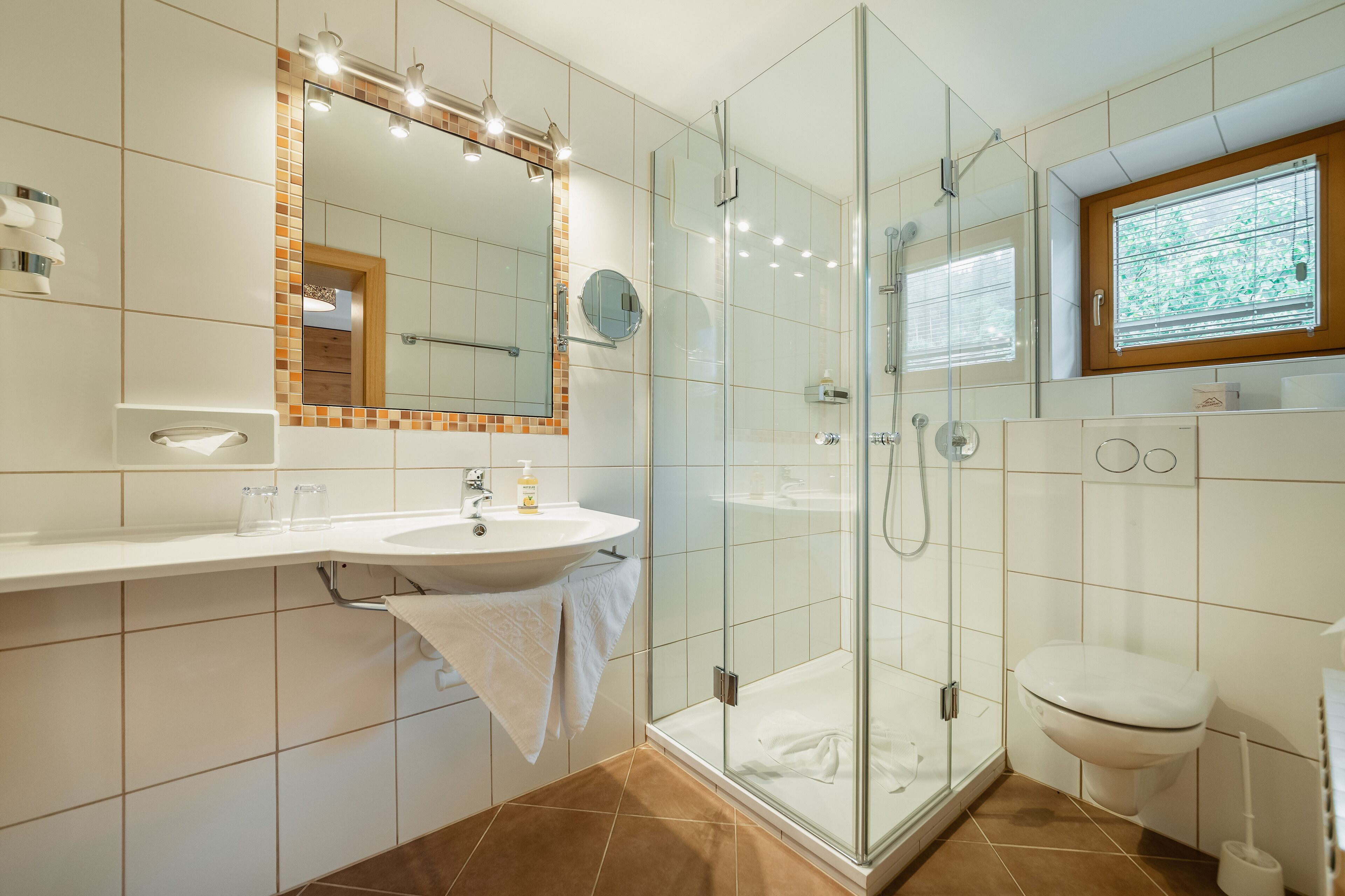 Ein modernes Badezimmer mit einer gläsernen Duschkabine, einem weißen Waschbecken mit Spiegel darüber und einer Toilette.