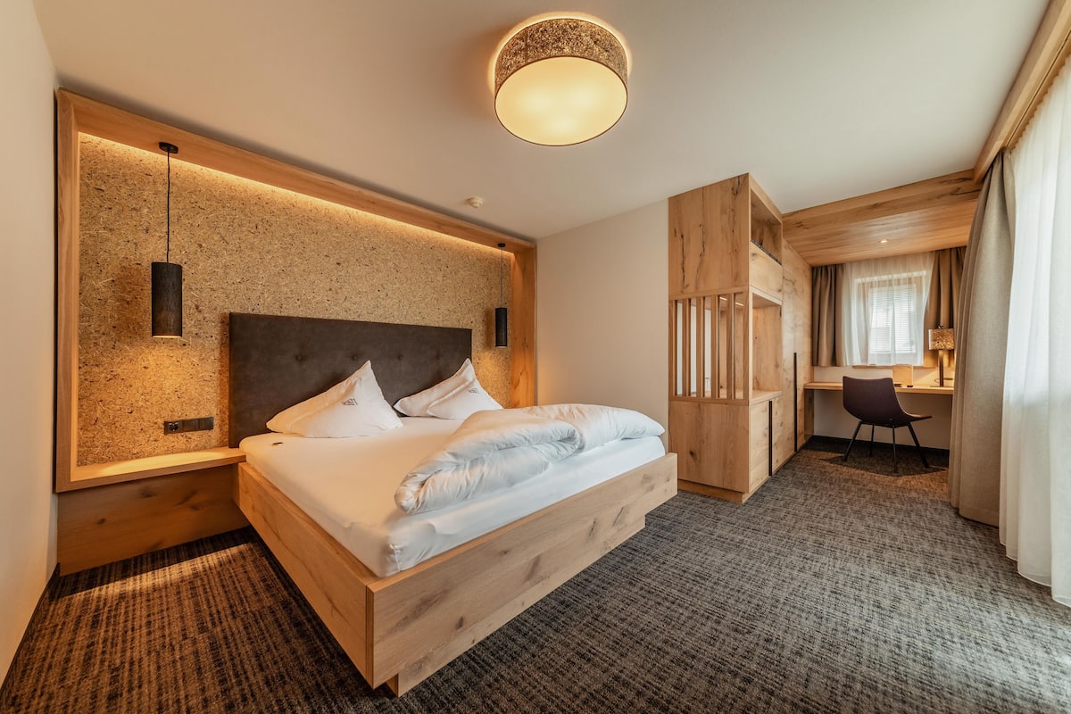 A modern hotel room with a wooden bed, a desk, and a large window with curtains.