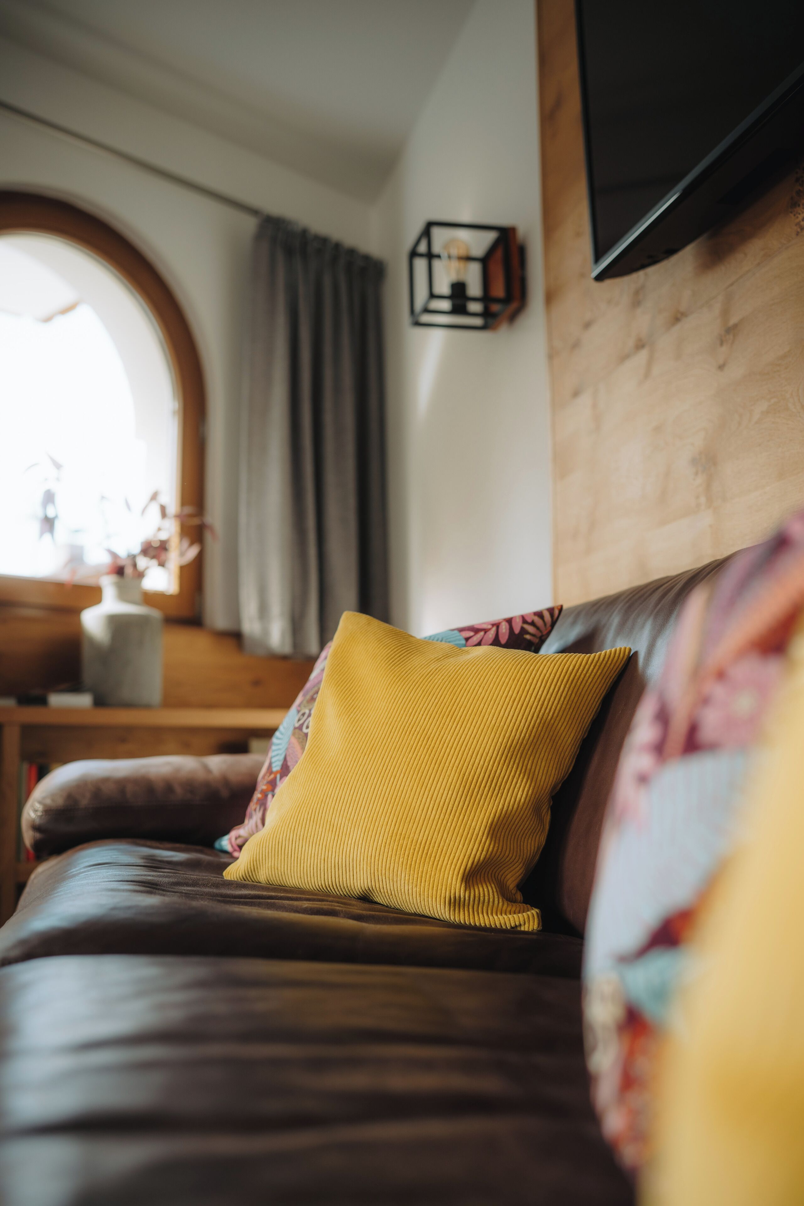 A room with a brown leather sofa, a yellow pillow, and a wooden wall.