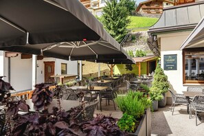 An outdoor seating area with tables and chairs, umbrellas, and potted plants.