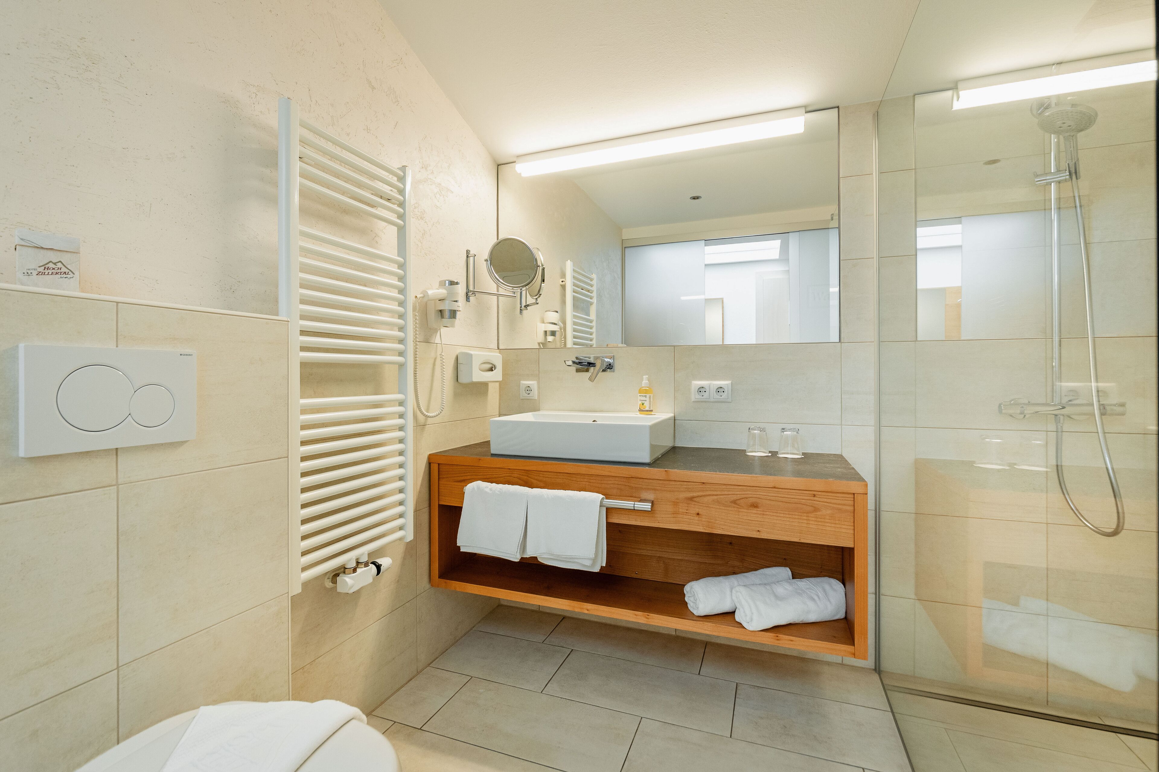 A modern bathroom with a white sink, wooden vanity, and a glass shower enclosure.