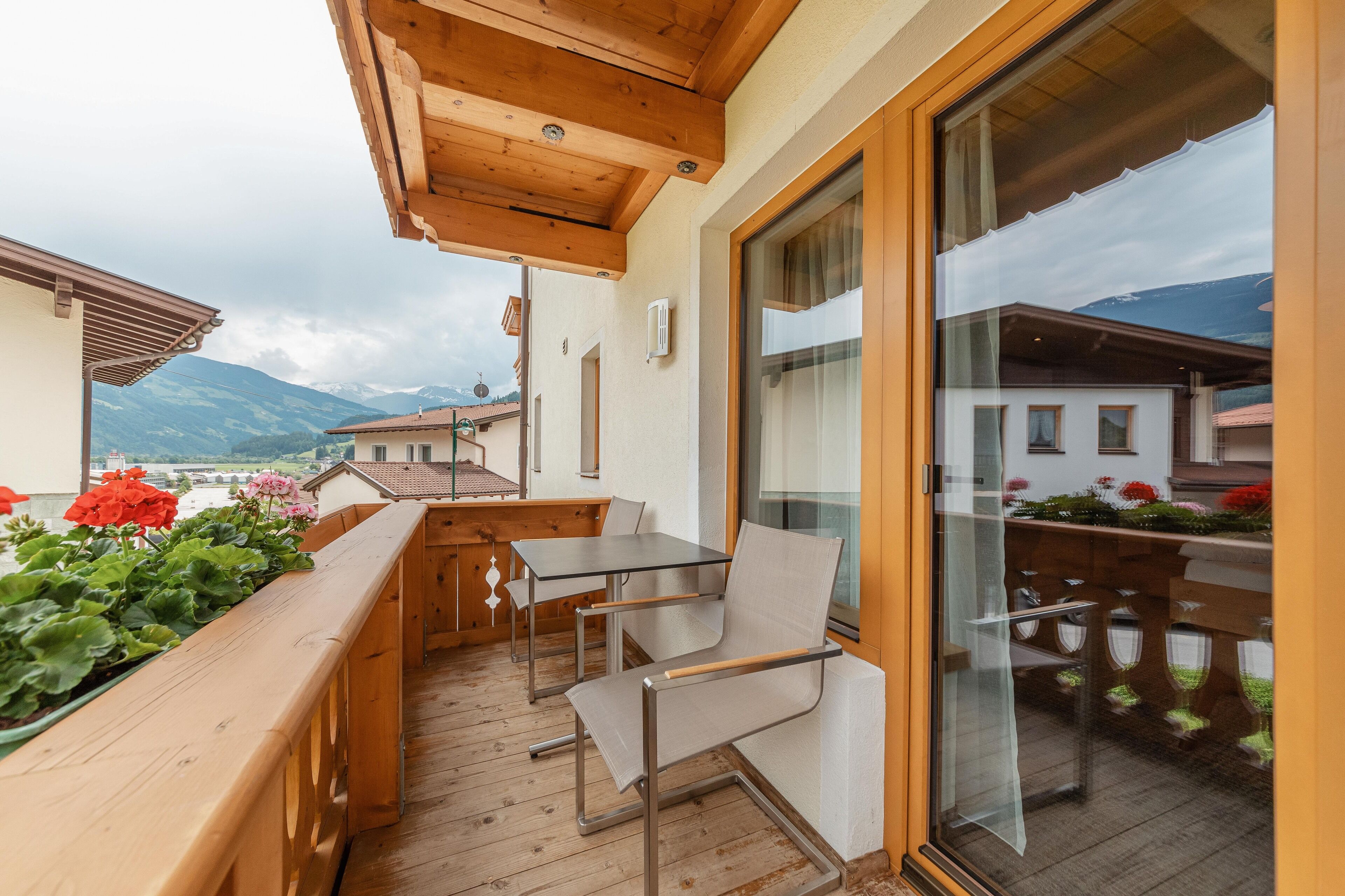 Una terraza de madera con una mesa, sillas, un vidrio y vistas a montañas.