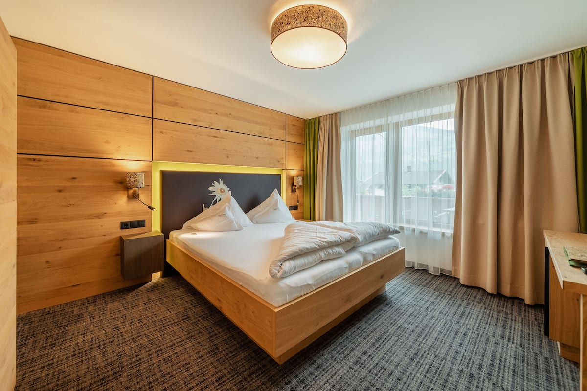 A modern hotel room with a wooden bed, a nightstand, and a desk with a lamp.