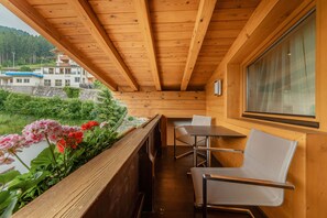 A wooden balcony with a table and chairs, overlooking a river and buildings. - Kräuterhotel Hochzillertal (Kaltenbach)
