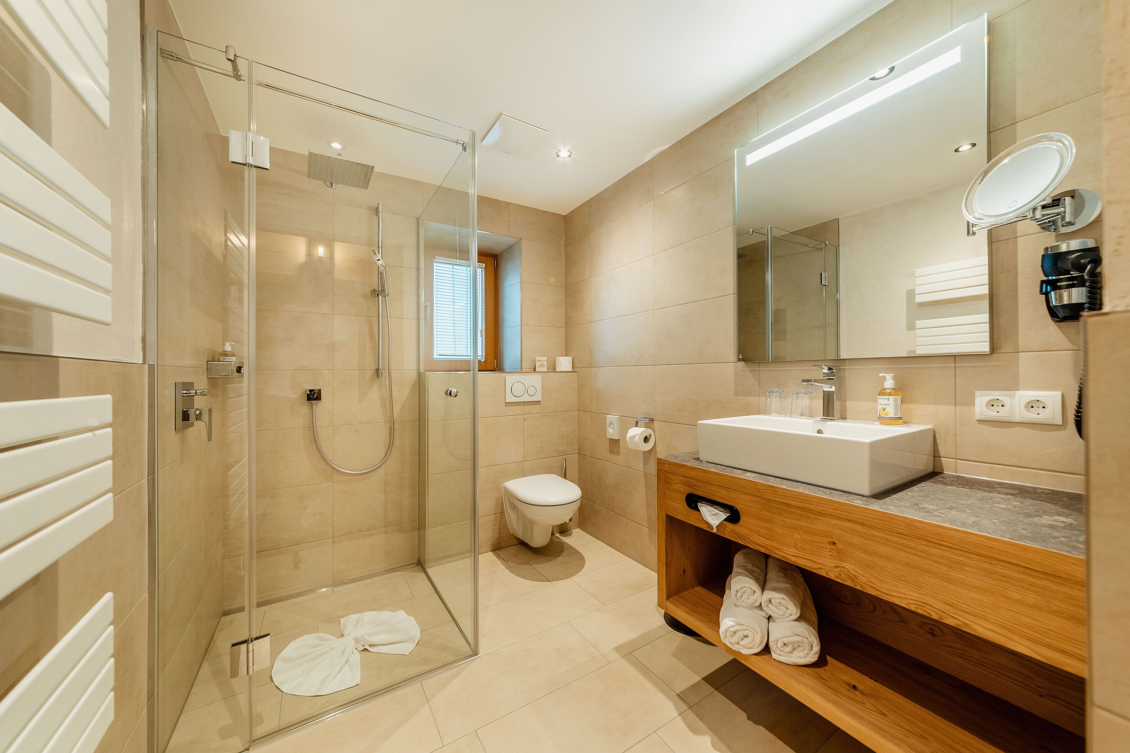 Un bagno moderno con doccia vetro, mobile lavabo in legno e un grande specchio.