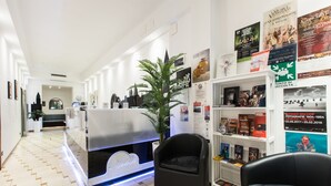 A modern hotel lobby with a reception desk, seating area, and a bookshelf with books and magazines. - Hotel Agli Artisti (Venice)