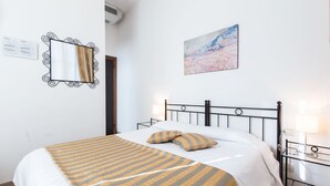 A neatly made bed with a striped bedspread and two pillows, a painting on the wall, and a small bedside table with a lamp. - Hotel Agli Artisti (Venice)