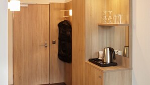 Habitación de hotel compacta con kitchenette, perchero y espejo.