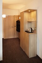 Quarto de hotel compacto com cozinha compacta, cabideiro e espelho.