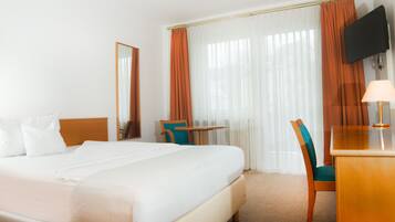 A hotel room with a bed, a desk, a chair, a TV, and a window with curtains.