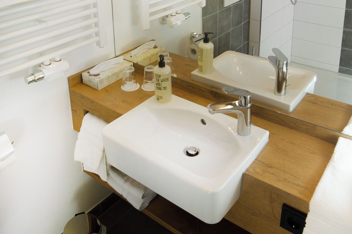 Ein modernes Badezimmer mit einem Holzbadezimmerhocker, einem Waschbecken, einem Spiegel und einer Dusche.