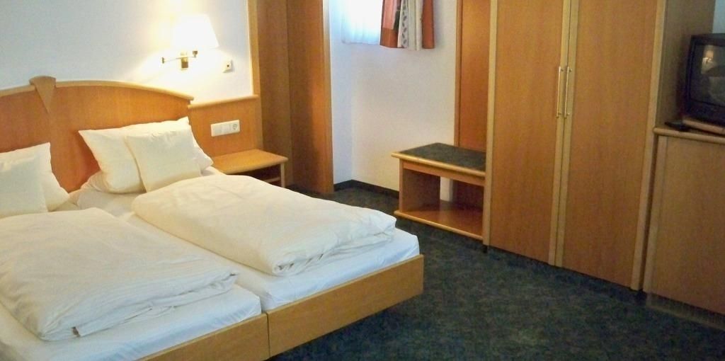 A hotel room with two beds, a nightstand, a small table, and a wardrobe.