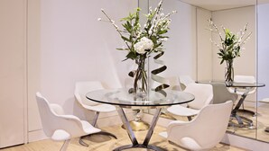 A modern dining area with a glass table, white chairs, and floral centerpieces. - No.5 Maddox Street (London)