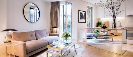 A modern living room with a sofa, coffee table, and a dining area with a kitchen in the background.