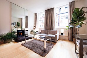 A modern living room with a sofa, a glass coffee table, a fireplace, and large windows with curtains. - No.5 Maddox Street (London)