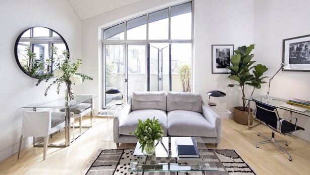 A modern living room with a glass coffee table, a grey sofa, a round mirror, and a large window offering a city view. - No.5 Maddox Street (London)