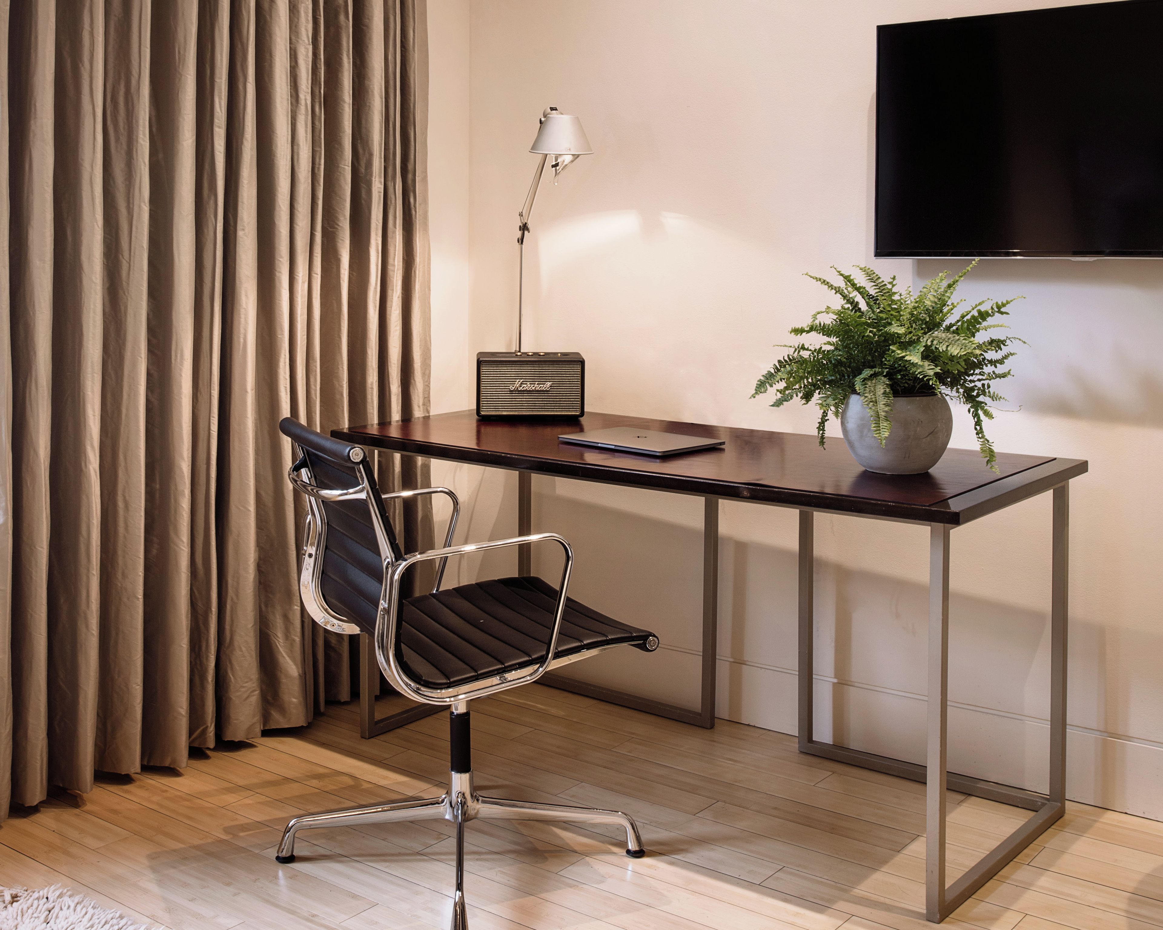 A modern office desk with a laptop, a Marshall speaker, a potted plant, and a chair.
