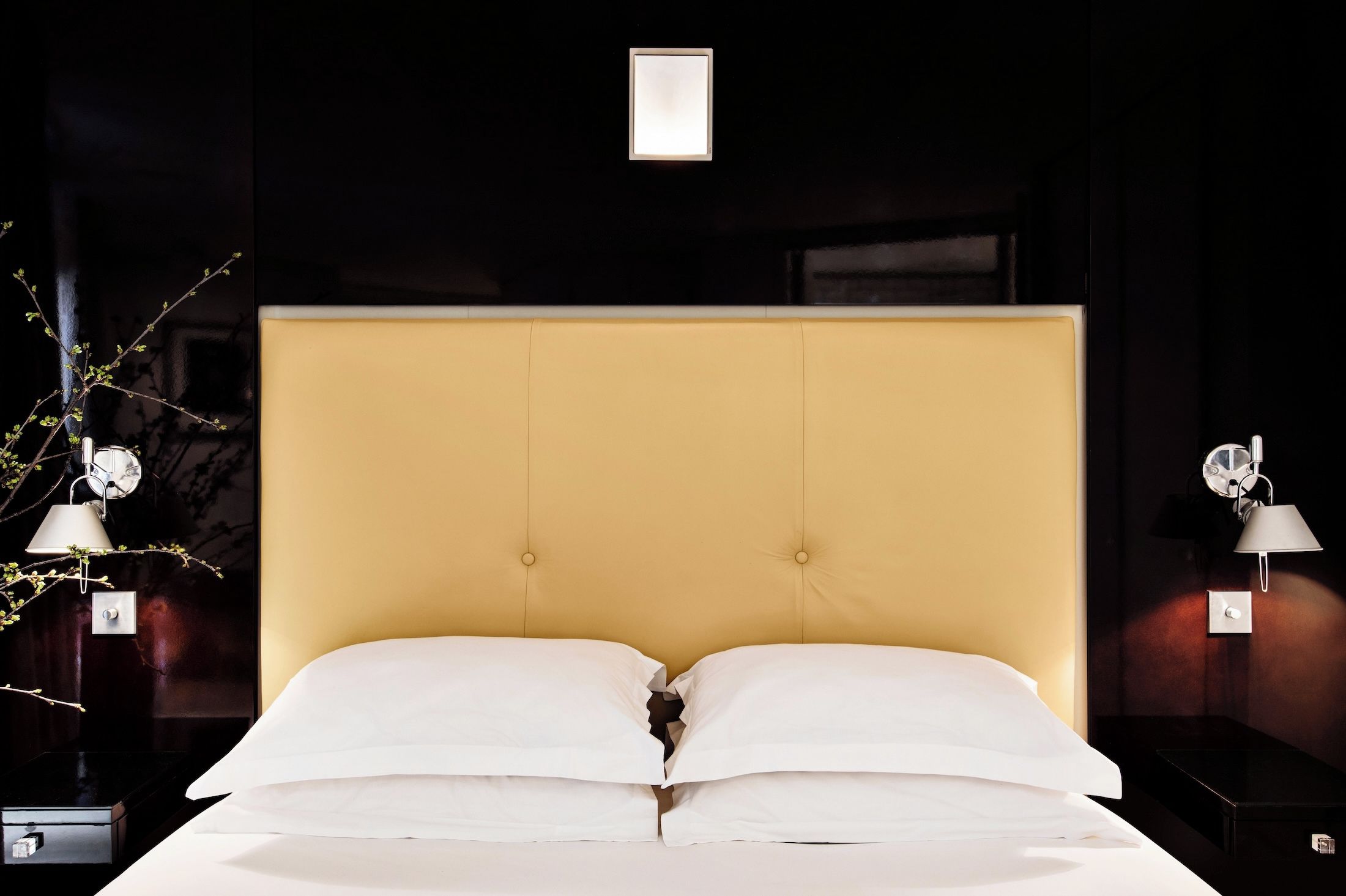 A bed with a headboard, two bedside tables with lamps, and a wall-mounted light fixture.