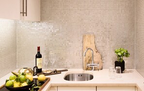 A kitchen with a stainless steel sink, a wooden cutting board, a potted plant, and a bowl of fruit. - No.5 Maddox Street (London)