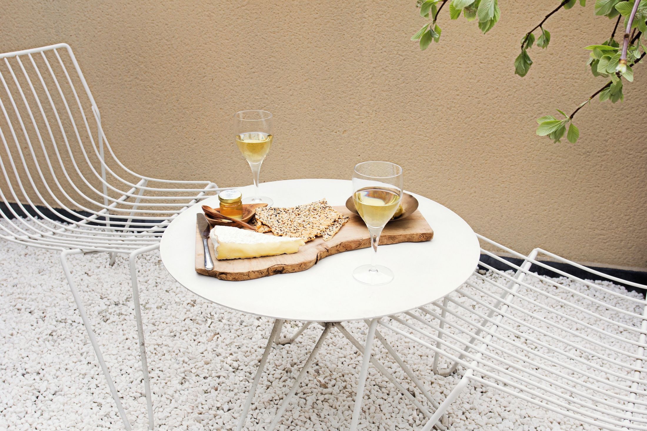 Ein runder Tisch mit weißer Tischdecke, zwei weiße Stühle, ein Teller mit Käse und Crackern sowie zwei Gläsern Weißwein.