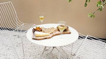 Ein runder Tisch mit weißer Tischdecke, zwei weiße Stühle, ein Teller mit Käse und Crackern sowie zwei Gläsern Weißwein.