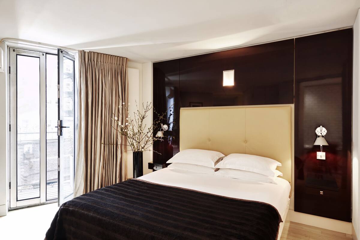 A hotel room with a large bed, a sliding glass door to the outside, a dark wooden headboard, and a nightstand with a lamp.