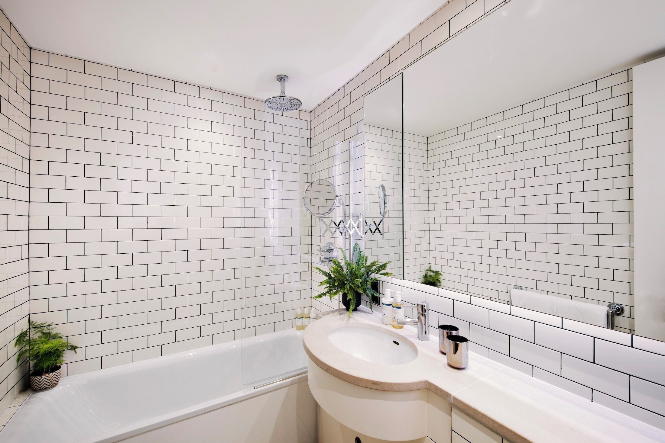 A bathroom with white subway tiles, a bathtub, a sink with a mirror, and a showerhead.