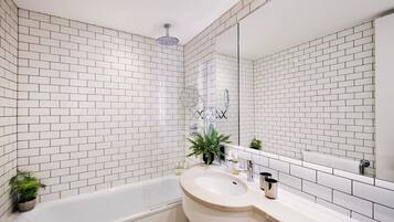 Un baño con azulejos blancos tipo metro, una bañera, un lavabo con espejo y un cabezal de ducha.