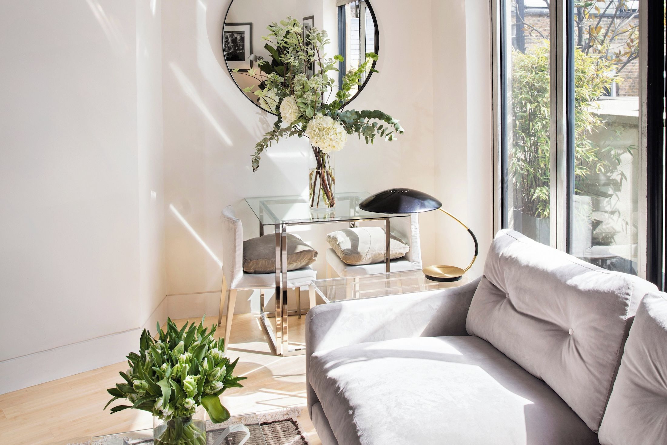 A modern living room with a sofa, a glass coffee table, a floor lamp, and a vase with flowers.