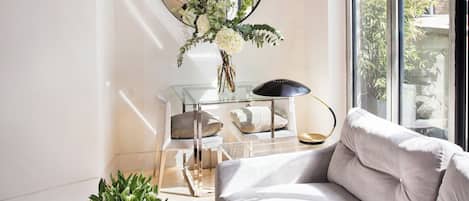 Un salon moderne avec un canapé, une table basse en verre, un lampadaire et un vase rempli de fleurs.