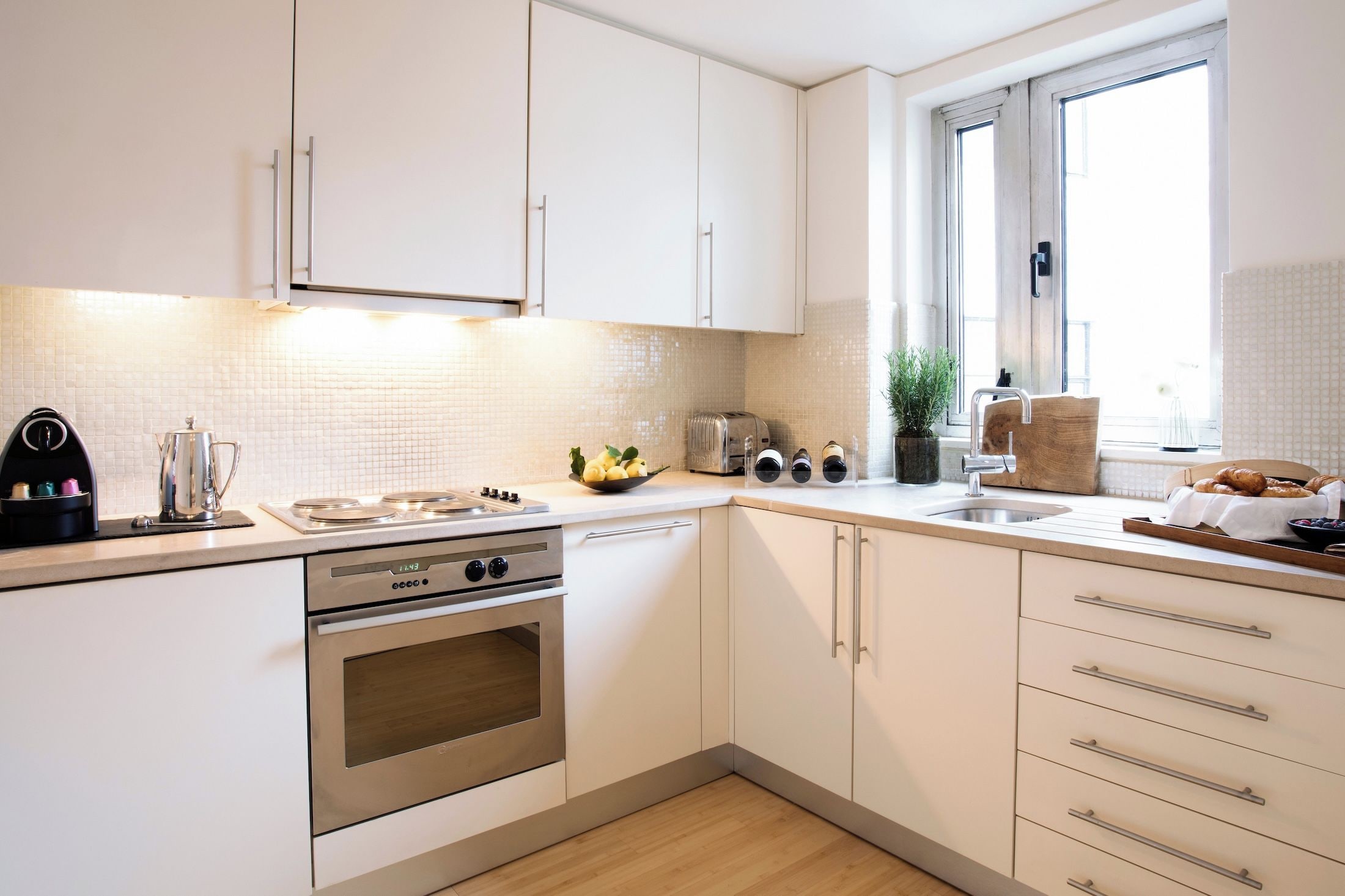 A modern kitchen with white cabinetry, a stainless steel stove, a toaster, and a sink.