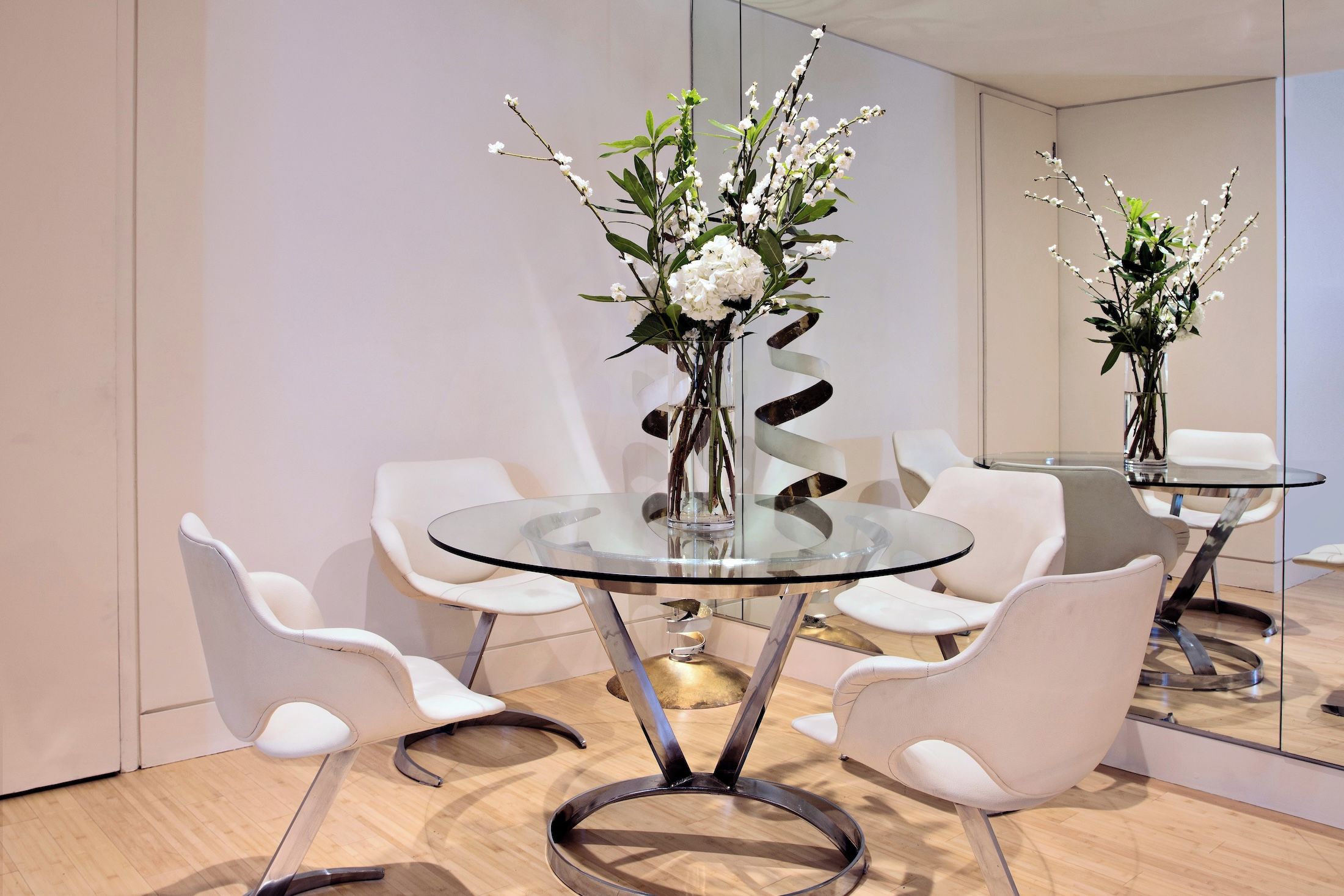 A modern dining area with a glass table, white chairs, and a vase with white flowers.