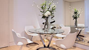 A modern dining area with a glass table, white chairs, and a vase with white flowers.