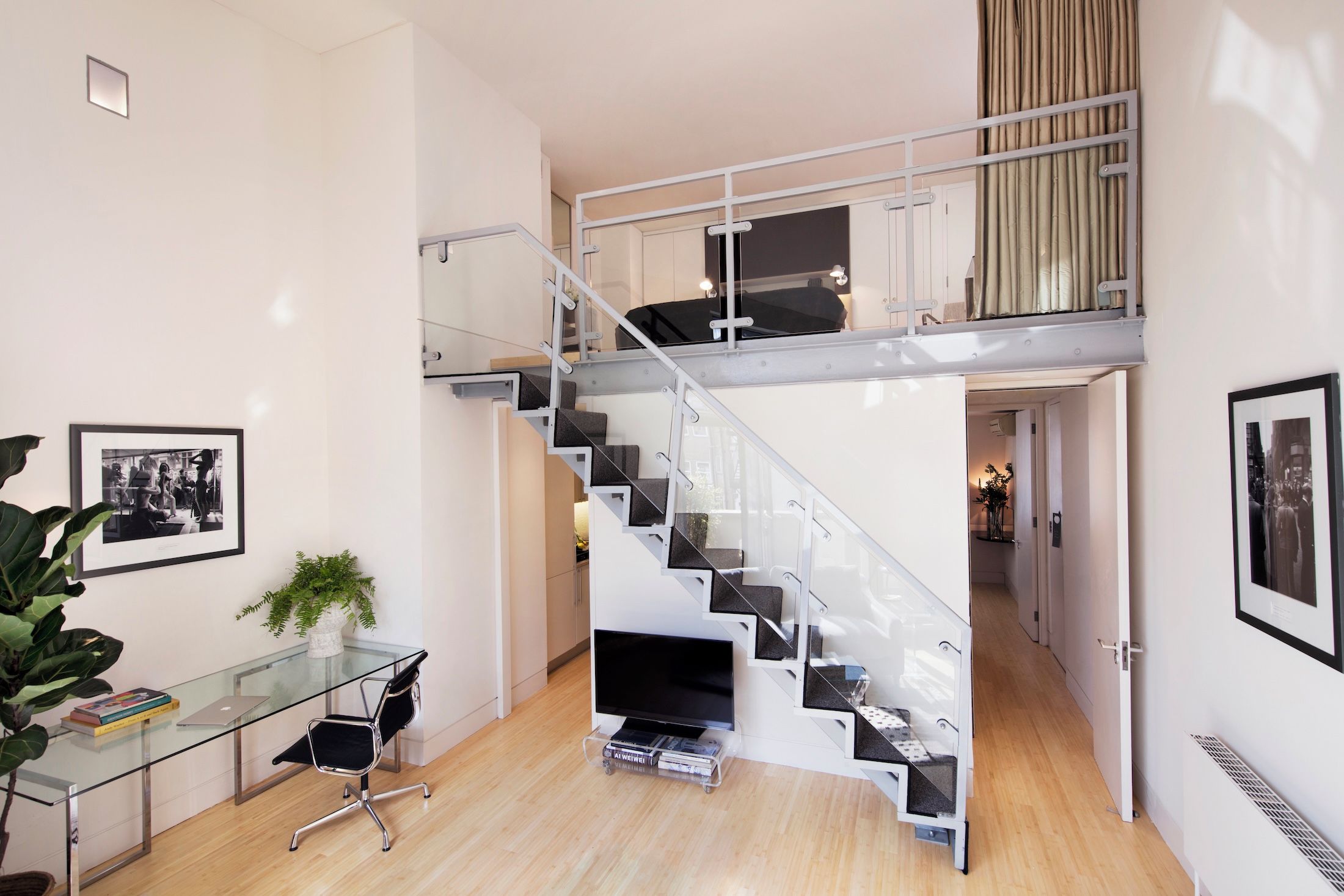 Ein modernes Interieur mit einem Glastisch, einem schwarzen Bürostuhl, einer Treppe mit Glastrennwand und einem Flachbildfernseher.