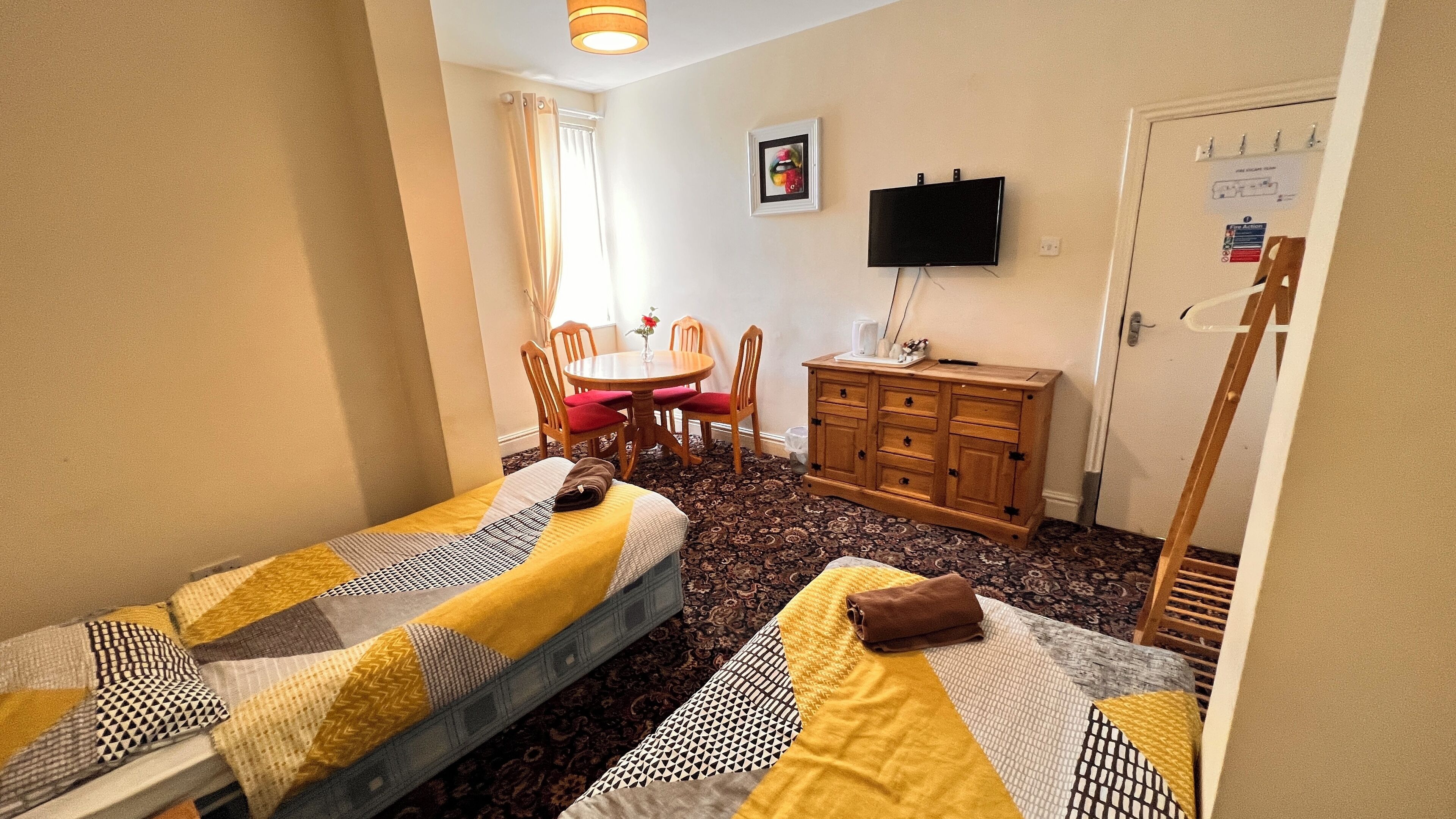 Una habitación pequeña y acogedora con dos camas individuales, un aparador de madera, un televisor y una mesa de comedor con sillas.