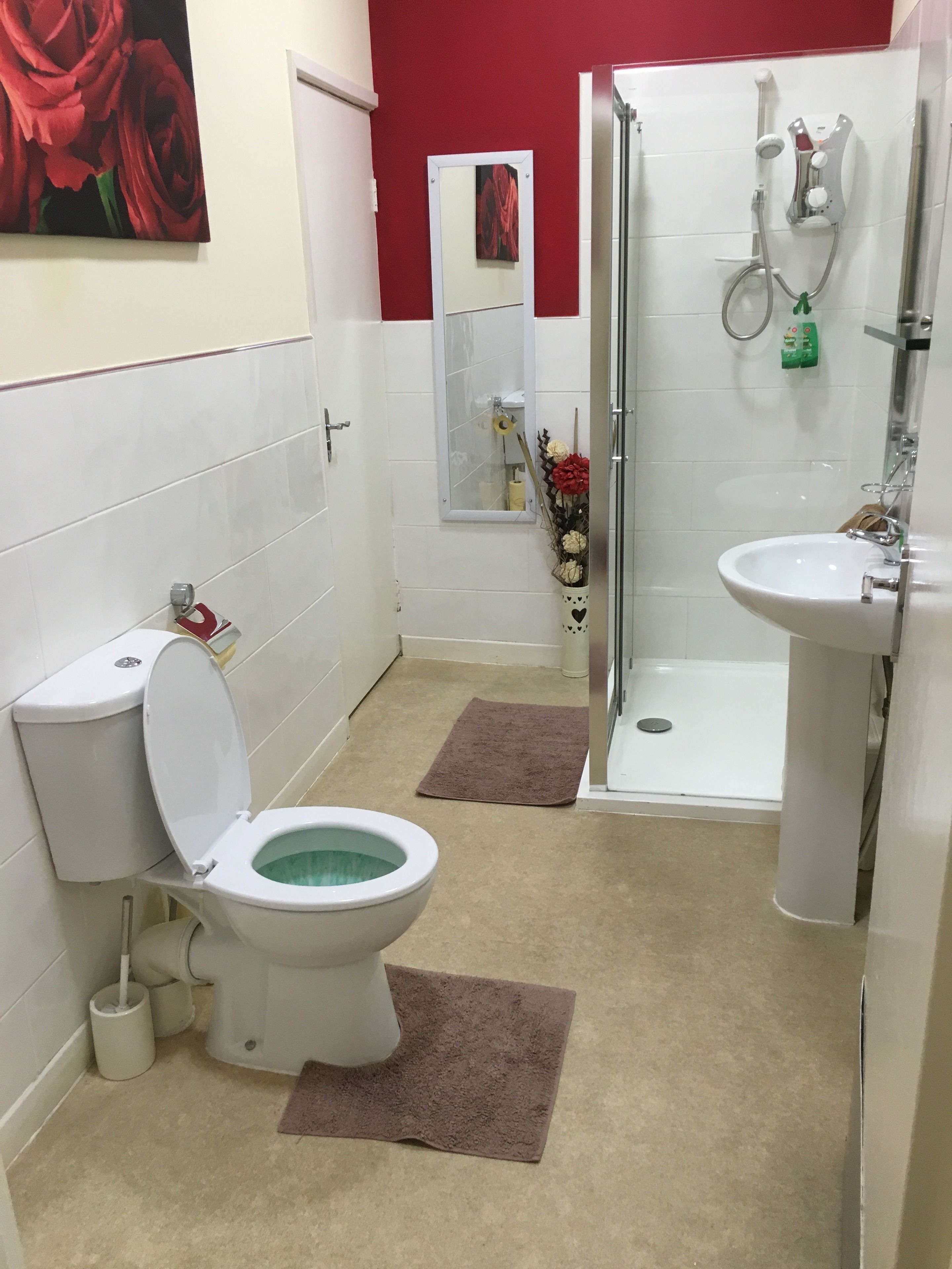 Casa de banho com sanita, lavatório, chuveiro e uma parede com detalhes em vermelho.