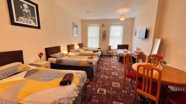 A hotel room with three beds, a desk, a chair, and a TV.