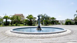 Una fuente circular con una estatua en el centro, rodeada por un área pavimentada con baldosas decorativas.