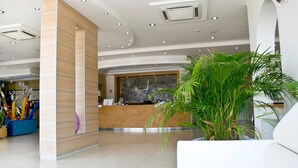 Un moderno vestíbulo de hotel con una recepción, una planta en maceta grande y un sofá blanco.