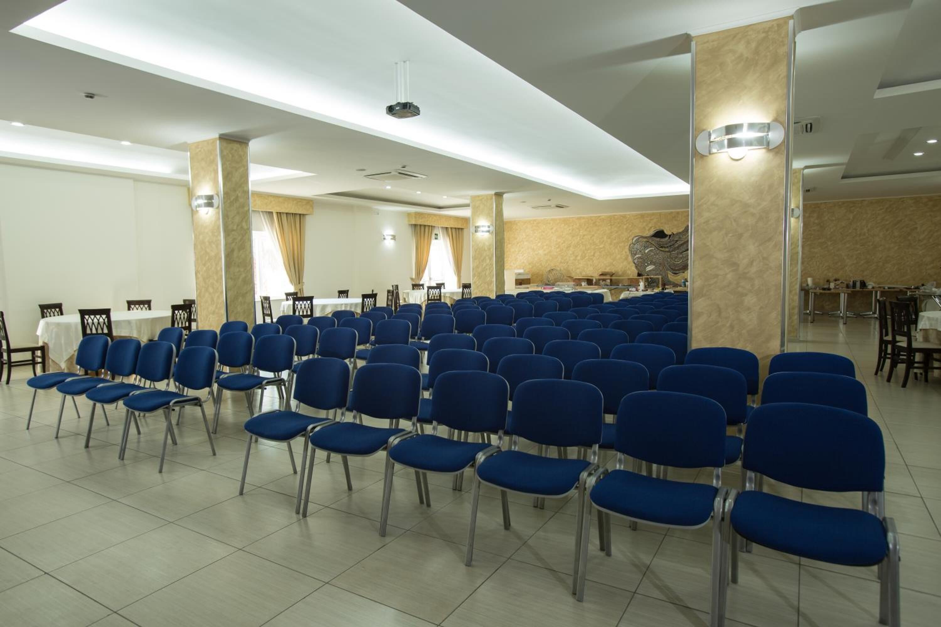 Ein Konferenzraum mit Reihen blauer Stühle, einer Bühne und einer großen Wanddekoration.