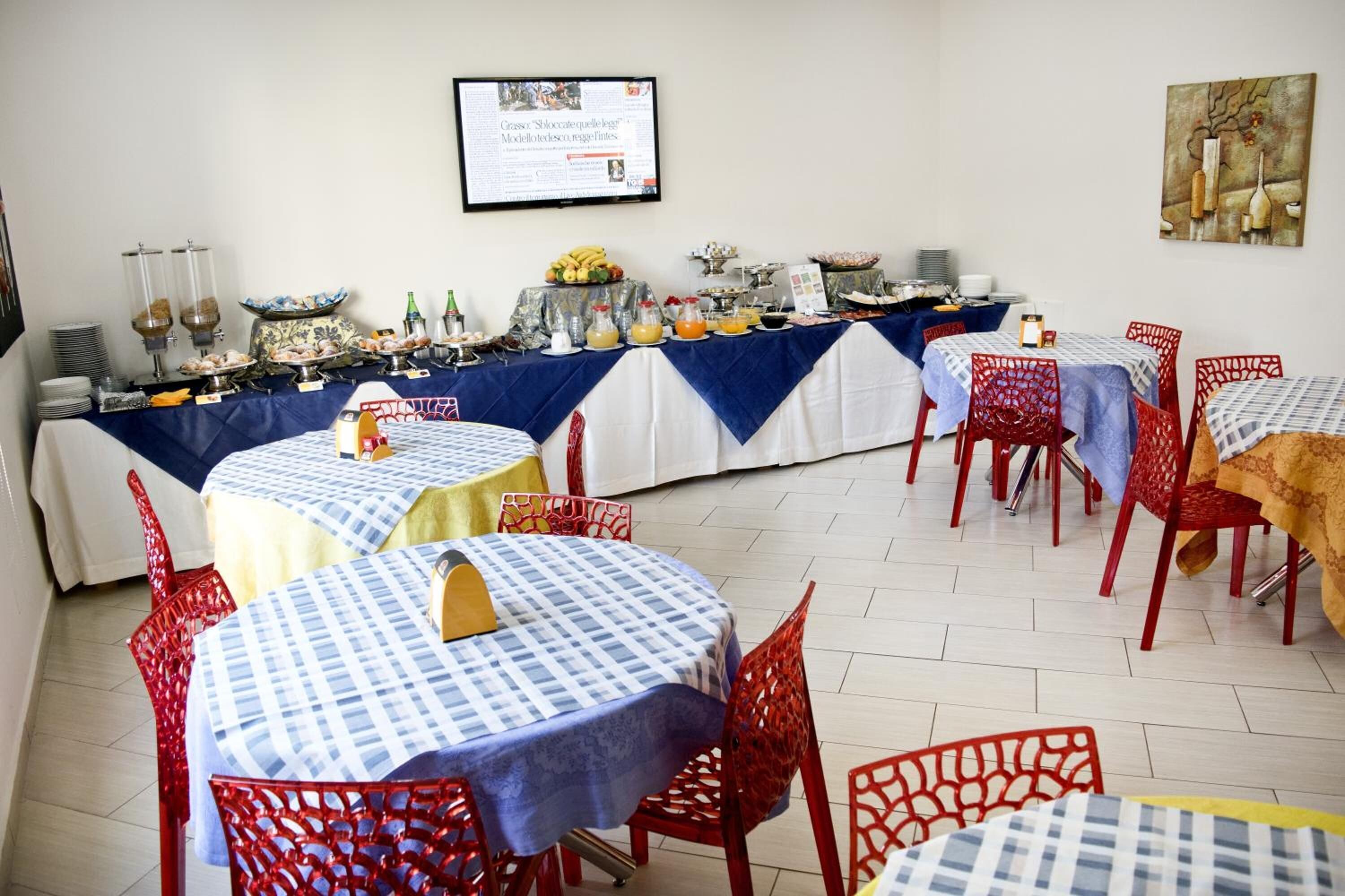 A dining area with round tables covered with blue and white checkered tablecloths, red chairs, and a buffet table with various food items and drinks.